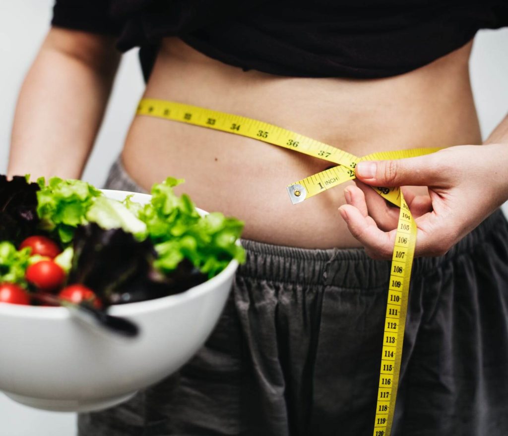 Woman Holding Salad in Bowl with Measuring tape around her belly